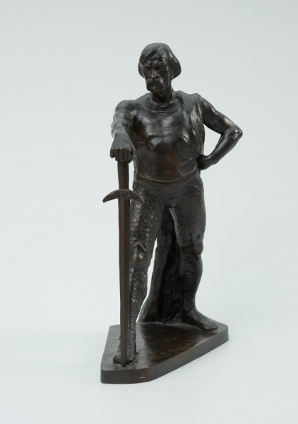 posąg - Ujęcie z przodu; Postać mężczyzny w postawie kroczącej. Wyciągnięta do przodu prawa ręka wsparta na mieczu. Wysunięta w prawo noga dotyka zakończenia ostrza miecza. Lewa ręka zgięta, dłoń wsparta na biodrze. Przez lewe ramię przewieszona draperia której zwój opada za lewą nogą do podstawy. Twarz pociągła, silnie zarysowane łuki brwi, usta okolone opadającym wąsem. Rozczesane gładko włosy.