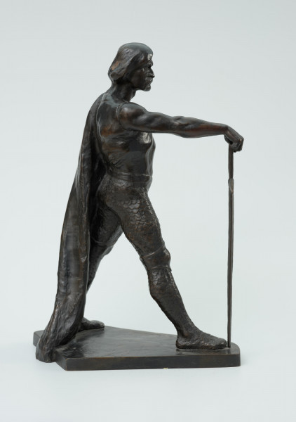 posąg - Ujęcie z boku z prawej strony;  Postać mężczyzny w postawie kroczącej. Wyciągnięta do przodu prawa ręka wsparta na mieczu. Wysunięta w prawo noga dotyka zakończenia ostrza miecza. Lewa ręka zgięta, dłoń wsparta na biodrze. Przez lewe ramię przewieszona draperia której zwój opada za lewą nogą do podstawy. Twarz pociągła, silnie zarysowane łuki brwi, usta okolone opadającym wąsem. Rozczesane gładko włosy.