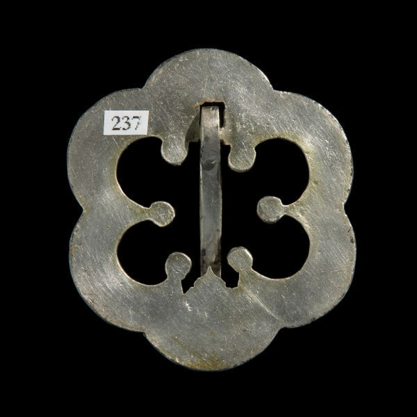 Pozłacana zapinka w kształcie rozety - Ujęcie z tyłu. Zapinka na planie sześciopłatkowej rozety. Od spodu gadka, w środku pusta. Kolec masywny, zwężający się.