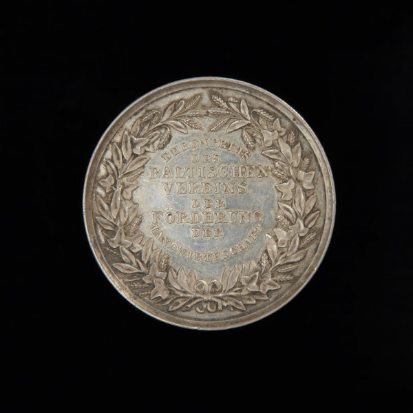 medal nagrodowy; nagroda honorowa - Ujęcie rewersu. Na rewersie w polu napis w 8 wierszach (górny wers łukiem wypukłym, dolny wklęsłym). W otoku wieniec z przeplecionych ze sobą kłosów i gałęzi bluszczu, przewiązanych u dołu wstążką.