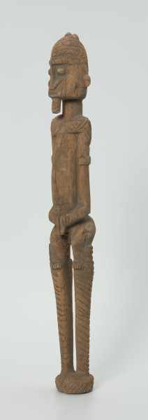 drewniana, rzeźbiona figura - Ujęcie z przodu, z lewej strony. Drewniana, rzeźbiona postać człowieka na szczudłach.