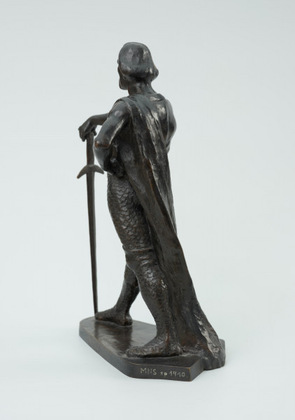 posąg - Ujęcie z tyłu skosem w lewą stronę; Postać mężczyzny w postawie kroczącej. Wyciągnięta do przodu prawa ręka wsparta na mieczu. Wysunięta w prawo noga dotyka zakończenia ostrza miecza. Lewa ręka zgięta, dłoń wsparta na biodrze. Przez lewe ramię przewieszona draperia której zwój opada za lewą nogą do podstawy. Twarz pociągła, silnie zarysowane łuki brwi, usta okolone opadającym wąsem. Rozczesane gładko włosy.