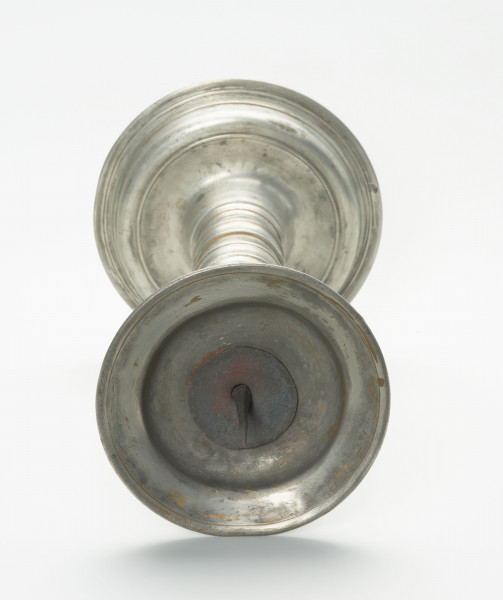 cynowy świecznik na okrągłej, wysklepionej stopie - Ujęcie od góry; Cynowy świecznik na okrągłej, wysklepionej stopie z profitką w formie talerzyka i iglicą do mocowania świecy. Iglica żelazna, kuta w formie czworobocznego ostrosłupa