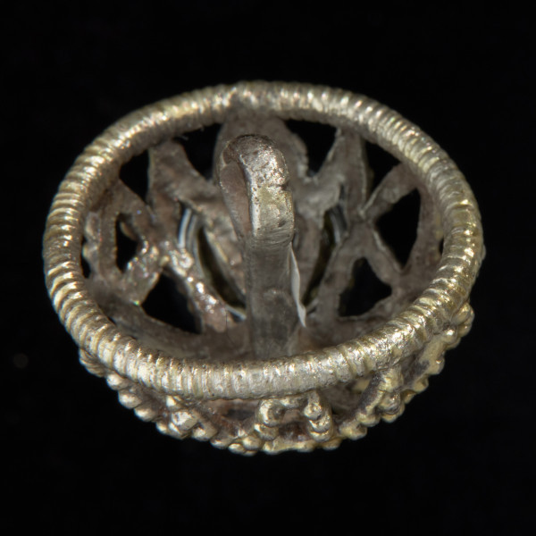 Pozłacany ażurowy guz koszyczkowy - Ujęcie z boku skosem do góry. Pozłacana okragła ozdoba, koszyczkowa, ażurowa, w formie kopułki.  Na wierzchołkach wypustki uformowane w oczka. Czterolistna rozeta wykonana jest z taśmy. W centrum nieregularny guzek.