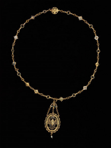 odznaka honorowa elektora saskiego Christiana II - Ujęcie całej odznaki z łańcuchem z przodu. Odznaka o owalnym kształcie, ażurowa, emaliowana. Na awersie pośrodku tarcza migdałowa z elektorskim herbem dzielonym. W otaczającym ją ornamencie na dwóch tabliczkach dewiza: A DEO / PRO IMPERIO. Nad inskrypcją oko opatrzności. Na rewersie w środkowym polu motyw słońca w otoczeniu sześciu gwiazd. Na tabliczkach inskrypcja: „TIME DEUM / HONORA CAESAREM”. U dołu zawieszenia sztyft będący pozostałością po perle. Odznaka przy pomocy trzech łańcuszków połączona jest z ażurową plakietką z uszkiem. Łańcuch składa się z 30 ozdobnych, ażurowych, emaliowanych ogniw, połączonych kółkami ze złotego drutu. Na połowie z nich ukazano emaliowane herby 15 prowincji saskich. Na pozostałych 15 przedstawiono serce z literą C i kapeluszem elektorskim, trzymane w dwóch dłoniach. Na kolistej zapince emaliowany herb elektorskiej Saksonii.