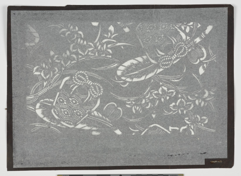 Szablon farbiarski katagami - Ujęcie z tyłu. Niewielki, zabarwiony na ciemnobrązowo, prostokątny szablon farbiarski typu jizomari, wzmocniona od spodu siatką z ludzkich włosów z negatywowo wyciętym wzorem. Na arkuszu o marginesach różnej wielkości przedstawiono motyw ozdobnych koszyków (jap. kagome) wśród irysów (jap. kakitsubata) i ptasich piór. Oś kompozycji przebiega diagonalnie od lewego dolnego narożnika do prawego górnego. Wszystkie trzy elementy dekoracyjne wycięto podwójnie, rozmieszczając je niesymetrycznie po obu stronach osi kompozycji. Na szablonie widoczne są uszkodzenia w postaci przerwanej siatki, szczególnie po prawej stronie kompozycji i przetarcia papieru. Od spodu zabezpieczony jest bibułą konserwatorską.