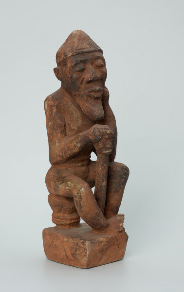 Ujęcie z przodu z prawej. Rzeźbiona w brunatno-czerwonym kamieniu dość duża postać mężczyzny (starca?) w pozycji siedzącej. Mężczyzna siedzi na okrągłym, malutkim stołku, ma charakterystyczne nakrycie głowy - spiczastą czapkę o zaokrąglonych rogach. Jego prawa ręka opiera się o berło (laskę) zakończone rzeźbą głowy. Widoczne rysy, mikropęknięcia i liczne malutkie otworki.