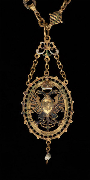 odznaka honorowa elektora saskiego Christiana II - Ujęcie z przodu z fragmentem łańcucha. Odznaka o owalnym kształcie, ażurowa, emaliowana. Na awersie pośrodku tarcza migdałowa z elektorskim herbem dzielonym. W otaczającym ją ornamencie na dwóch tabliczkach dewiza: A DEO / PRO IMPERIO. Nad inskrypcją oko opatrzności. Na rewersie w środkowym polu motyw słońca w otoczeniu sześciu gwiazd. Na tabliczkach inskrypcja: „TIME DEUM / HONORA CAESAREM”. U dołu zawieszenia sztyft będący pozostałością po perle. Odznaka przy pomocy trzech łańcuszków połączona jest z ażurową plakietką z uszkiem. Łańcuch składa się z 30 ozdobnych, ażurowych, emaliowanych ogniw, połączonych kółkami ze złotego drutu. Na połowie z nich ukazano emaliowane herby 15 prowincji saskich. Na pozostałych 15 przedstawiono serce z literą C i kapeluszem elektorskim, trzymane w dwóch dłoniach. Na kolistej zapince emaliowany herb elektorskiej Saksonii.