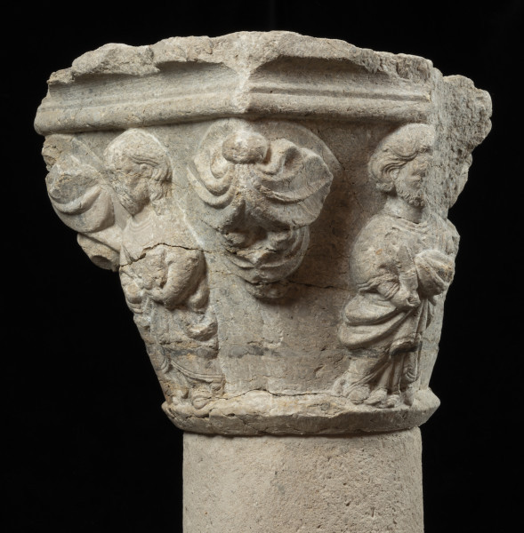 kapitel z przedstawieniem czterech apostołów - Ujęcie trzeciego narożnika z liśćmi palmetowymi, po bokach apostołowie. Kapitel blokowo-kielichowy, rozszerzający się ku górze, wykuty z jednego kawałka kamienia. Okrągłą podstawę otacza wałek o profilu trójkątnym. Zwieńczenie w formie szerokiej czworobocznej płyty abakusa o krawędziach profilowanych wałkiem i wklęską. Na osi każdego boku półplastyczne przedstawienie frontalnie ukazanych postaci Apostołów: Piotra, Pawła, Bartłomieja i Jakuba Starszego. Pomiędzy nimi duże liście palmetowe dekoracyjnie ułożone na narożnikach. Postaci o dużych głowach i dość smukłej budowie, trzymają atrybuty. Długie tuniki i płaszcze o pofałdowanej powierzchni przylegają do sylwetek. Charakterystyczne zdobienie krawędzi szat podwójnym wałkiem i symetrycznie ułożone falujące fryzury. Relief półplastyczny, światłocieniowy. Tło opracowane gładko. Jedno z naroży kapitela uszkodzone. Liczne pęknięcia i ukruszenia na powierzchni kamienia. Pod spodem centralne wgłębienie do umocowania trzpienia łączącego kapitel z trzonem.