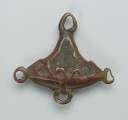biżuteria, ozdoba - Ujęcie z tyłu. Mały, trójkątny, ozdobiony wzorami geometrycznymi wisiorek, wykonany z brązu. W jego dolnej części udekorowany został trzema małymi, pustymi wewnątrz kółeczkami (jedno lekko zdeformowane). W jego górnej części wykonano owalny otwór. Widoczne ślady użytkowania, lekko wytarty wzór.