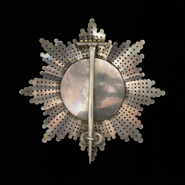 Gwiazda Orderu Świętego Stanisława I klasy - Ujęcie z tyłu. Ośmioramienna gwiazda o groszkowanych promieniach z dewizą orderu i okrągłą plakietką z inicjałami SS. Na rewersie szpila z uszkiem do zapięcia.