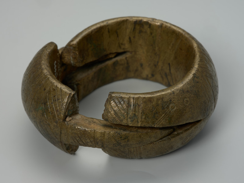 biżuteria, bransoleta - Ujęcie z tyłu z góry rozpiętej bransolety. Dwuczęściowa, mosiężna, kulista bransoleta składająca się z dwóch wkładanych, półkulistych elementów. Zewnętrzna powierzchnia ozdobiona punktowym wzorem w postaci pionowych i ukośnych linii, kół oraz półkoli. Brak wzoru na bocznym grzebiecie.