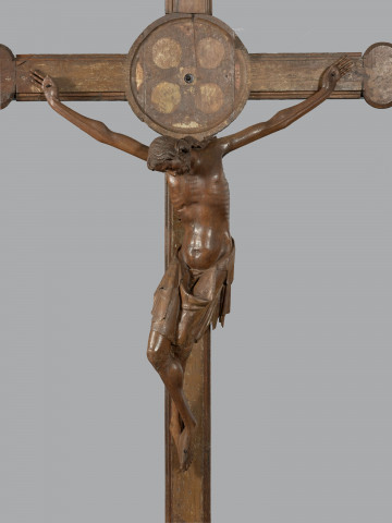 MNS/Szt/45 krucyfiks kamieński - figura - Ujęcie z przodu; Ponadnaturalnych rozmiarów figura Chrystusa Ukrzyżowanego. Smukłe, wyidealizowane ciało o nieco wydłużonych proporcjach ułożone w esowaty kształt. Długie ręce rozłożone szeroko w formie rozciągniętej litery V. Dłonie ułożone płasko, zwrócone wnętrzem, o długich wyprostowanych palcach. Głowa zwieszona nisko przy prawej piersi. Miękko rzeźbiona twarz o zamkniętych oczach, długim nosie i lekko ściągniętych brwiach. Finezyjnie ułożona fryzura falujących włosów. Długi tors o łagodnym zarysie wypukłej klatki piersiowej, wklęsłej jamy brzusznej i kolistego brzucha. Szczupłe nogi skrzyżowane prawa nad lewą. Na biodrach chusta perizonium sięgająca kolan. W dłoniach i w skrzyżowanych stopach otwory na gwoździe. Korpus figury wykonany w jednym kawałku drewna. Ręce mocowane na trzpień w otwory w barkach. Na odwrociu torsu dwa metalowe oczka do zawieszenia figury na krzyżu. Chusta wtórnie skrócona z prawej strony, stopy uzupełnione.