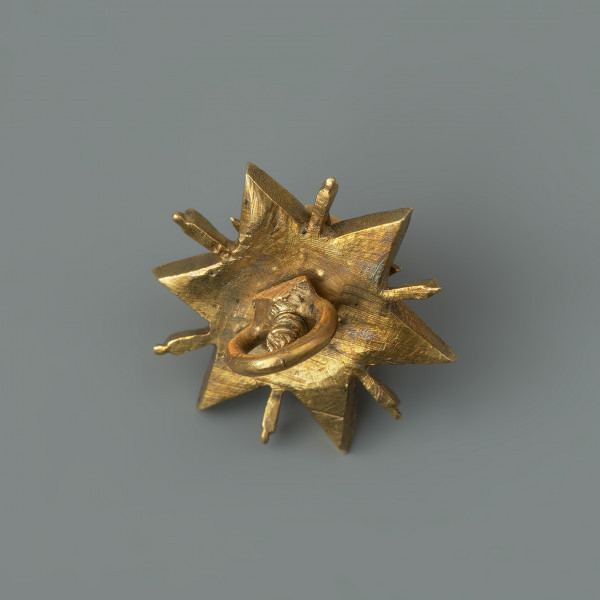 pontalik w kształcie gwiazdki - Ujęcie z tyłu. Podstawa w kształcie sześcioramiennej gwiazdki, kameryzowanej diamentami o szlifie rozetowym. Ramiona gwiazdki rozdzielone wąskimi promieniami pokrytymi białą emalią. W górnej części rozetka z sześciu lancetowatych liści, na niej zwieńczenie w formie kasztu z niezachowanym kamieniem. Poszczególne części połączone śrubą. Na spodzie uszko służące do mocowania klejnotu do stroju.