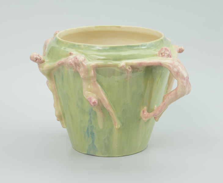 ceramika - ujęcie boku kolejne; Postać na wprost obrócona głową w lewa stronę ze zgiętym prawym kolanem. Postacie po bokach trzymają kobietę za ręce. Postacie porcelanowe przyczepione do wazonu w kolorze zielonym.