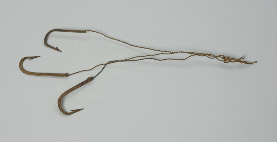 haczyki - 3 szt. - Ujęcie przodu haczyków z góry. Haczyk (3 szt.). Wyrób fabryczny, wykonany z mosiądzu.  Trzonek haczyka prosty, spłaszczony, bez dodatkowych zadziorów z niewielkim oczkiem, w którym mocowany jest wykonany ze skręconego drutu, przypon. Grot prosty (znajdujący się w jednej płaszczyźnie z trzonkiem), ze znajdującym się po jego wewnętrznej stronie zadziorem.