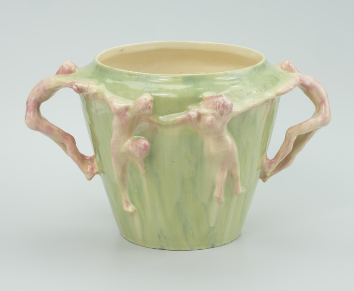 ceramika - Ujęcie kolejnego boku; Widoczne dwie postacie na wprost, trzymające się za ręce, mężczyzna z lewej skierowany przodem w nasza stronę natomiast kobieta z prawej strony skierowana tyłem do widza. Trzymają za swoje ręce po bokach kolejne postacie opierające się na głowach i stapach z wygiętym tułowiem do tyłu.