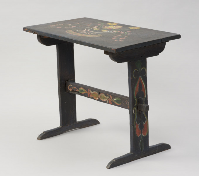 meble - Ujęcie ze skosu z drugiej strony; Stół z malaturą kwiatową na blacie i desce łączącej nogi. Blat prostokątny, wsparty na dwóch wspornikach/nogach w kształcie odwróconej litery 