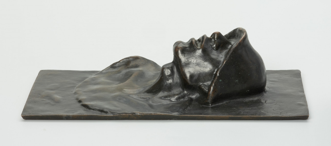 portret męski - Ujęcie w poziomie z praej strony; Płaskorzeźba przedstawiająca głowę mężczyzny. Z blachy stanowiącej tło wyłania się kwadratowa twarz z szerokim nosem i rozchylonymi ustami, szyja mocno osadzona, szeroka. Na głowie hutniczy kask. Widoczny fragment torsu.