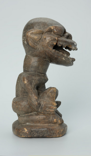 rzeźba; przedmiot obrzędowy; Figura kultu zmarłych - Ujęcie prawy bok. Rzeźbiona w grafitowym steatycie, usadowiona na płaskiej, owalnej podstawie postać siedzącego z podkurczonymi nogami mężczyzny o masywnej głowie i tęgiej szyi z odsłoniętymi genitaliami. Powierzchnia rzeźby niejednolita; ubytek na prawym kolanie; ślady klejenia na twarzy.
