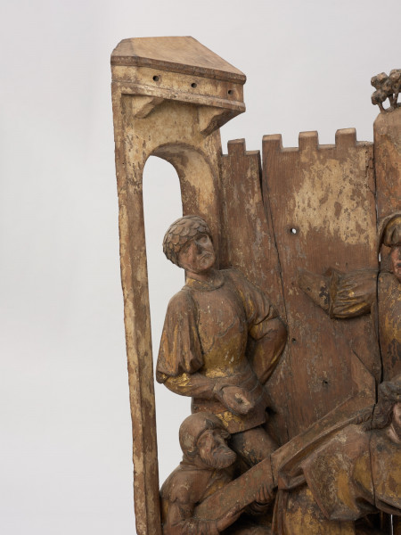 sztuka sakralna, kwatera ołtarza, płaskorzeźba - detal; Płaskorzeźba przedstawiająca Chrystusa pochylonego pod ciężarem krzyża oraz pomagającego mu na rozkaz żołnierzy Szymona Cyrenejczyka. Scena na tle pejzażu górskiego przed murami miasta. Kwatera środkowa późnogotyckiego ołtarza pasyjnego z Wkryujścia (Ueckermünde).