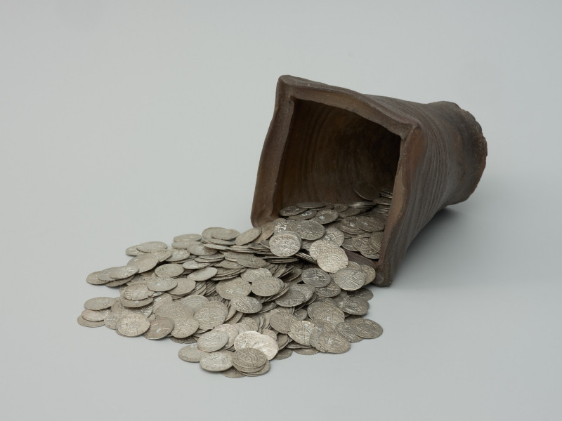 Ujęcie naczynia z wysypującymi się monetami z przodu skosem w lewo. Skarb 656 szelągów krzyżackich i 2 guldenów niemieckich ukryty w kaflu piecowym pod koniec XV wieku.