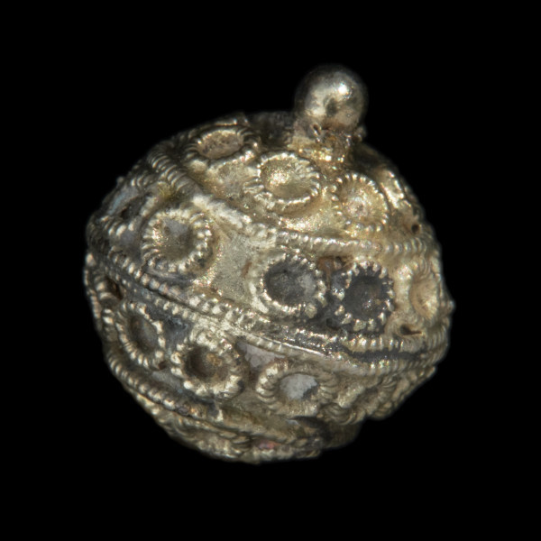 Pozłacany guz kulisty - Ujęcie z przodu, pod skosem w prawo. Pozłacana ozdoba kolista; na blaszanej połówce pasma kółeczek, rozdzielonych pierścieniami z perełkowanego drutu. Na górze, na środku okrągła granulka.