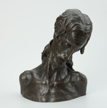 scena religijna - Ujęcie z przodu; Rzeźba przedstawiająca głowę mężczyzny pochyloną skosem do przodu. Długie, lekko kręcone włosy do ramion, wysokie wypukłe czoło, wąski, długi nos, wąsy i broda.  Głowa umęczonego Chrystusa.