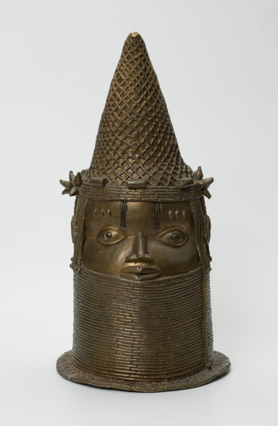 Głowa Królowej Matki - Ujęcie z przodu. Brązowy, pusty w środku odlew głowy kobiety, o złotym zabarwieniu. Twarz o cechach negroidalnych, wydatnych, lekko rozchylonych ustach oraz szerokim u nasady nosie ma oczy z wyraźnie zaznaczoną linią powiek. Na ich wysokości usytuowane są nieduże uszy. Lekko wypukłe czoło dekorowane jest pionowymi inkrustacjami z żelaza oraz trzema podłużnymi, symetrycznie rozmieszczonymi, pogrubieniami nad każdym okiem. Szyję i podbródek do wysokości dolnej wargi zasłonięto masywnym naszyjnikiem z korali. Głowa jest nienaturalnie poszerzona w tylnej części, tuż pod przechyloną do przodu koroną o charakterystycznym kształcie dziobu papugi, którą nad uszami ozdobiono dwoma rozetami. W dolnej części korony widnieje pięć ozdób o walcowatej formie, trzy nad czołem, dwie za rozetami oraz opaska z korali. Tuż za koroną znajduje się duży, owalny otwór na rzeźbiony kieł słonia, którego brak. Poniżej, po obu stronach twarzy i z tyłu głowy, zaznaczono zaplecione w warkoczyki włosy. Z tyłu głowy pomiędzy włosami a naszyjnikiem usytuowany jest niewielki, okrągły otwór. U podstawy odlewu znajduje się pozioma listwa, dekorowana motywem plecionki.