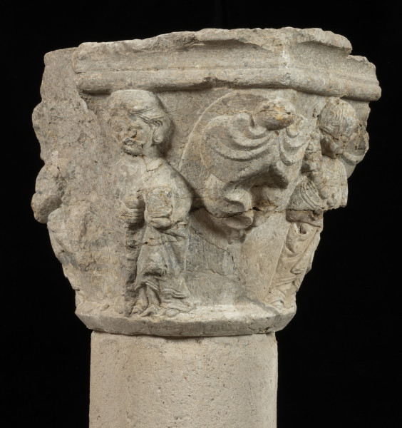 kapitel z przedstawieniem czterech apostołów - Ujęcie drugiego narożnika z liśćmi palmetowymi. i uszkodzonym bokiem. Kapitel blokowo-kielichowy, rozszerzający się ku górze, wykuty z jednego kawałka kamienia. Okrągłą podstawę otacza wałek o profilu trójkątnym. Zwieńczenie w formie szerokiej czworobocznej płyty abakusa o krawędziach profilowanych wałkiem i wklęską. Na osi każdego boku półplastyczne przedstawienie frontalnie ukazanych postaci Apostołów: Piotra, Pawła, Bartłomieja i Jakuba Starszego. Pomiędzy nimi duże liście palmetowe dekoracyjnie ułożone na narożnikach. Postaci o dużych głowach i dość smukłej budowie, trzymają atrybuty. Długie tuniki i płaszcze o pofałdowanej powierzchni przylegają do sylwetek. Charakterystyczne zdobienie krawędzi szat podwójnym wałkiem i symetrycznie ułożone falujące fryzury. Relief półplastyczny, światłocieniowy. Tło opracowane gładko. Jedno z naroży kapitela uszkodzone. Liczne pęknięcia i ukruszenia na powierzchni kamienia. Pod spodem centralne wgłębienie do umocowania trzpienia łączącego kapitel z trzonem.