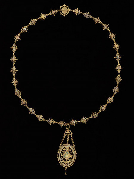 odznaka honorowa elektora saskiego Jana Jerzego I - Ujęcie odznaki z tyłu z łańcuchem. Odznaka o owalnym kształcie, ażurowa, emaliowana. Jej głównym elementem jest czarny dwugłowy orzeł w koronie cesarskiej. Na awersie, na piersi orła herb Saksonii Elektorskiej. W owalnej ramce, otoczonej rucianym wieńcem inskrypcja: SVB. VMBRA. ALARUM. TUARUM.1.6.11. Na rewersie na tułowiu orła wieniec z kwiatkami trzymany przez dwie dłonie. W otoku napis: PRVS. MOR. QVAM. FIDEM. FALLIERE. U dołu szczątkowo zachowana perła. Odznaka przy pomocy trzech łańcuszków połączona jest z ażurową plakietką z uszkiem. Łańcuch składa się z dziesięciu owalnych ogniw z emaliowanymi herbami prowincji saskich (różnymi po obu stronach). Między nimi ogniwa z motywem dłoni trzymających zielony wieniec z białymi kwiatkami, a także gładkie okrągłe ogniwa i ogniwa o fakturze plecionki. Na emaliowanej, kolistej zapince motyw dwugłowego orła z herbem Saksonii Elektorskiej.