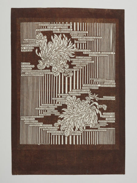 szablon farbiarski katagami; wycinanka; dekoracja - Ujęcie z przodu. Duży, zabarwiony na brązowo, prostokatny szablon farbierski typu jizomari, przedstawiający chryzantemy otoczone motywem stylizowanych chmur na tle pionowych pasków.