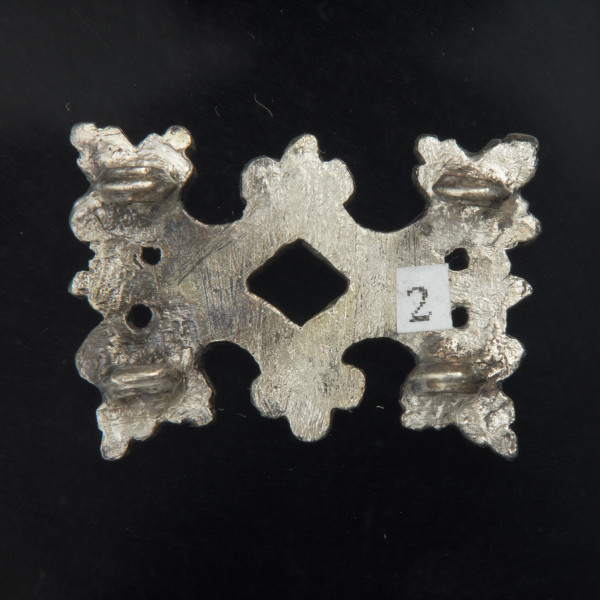 Pozłacane okucie pasa z ornamentem roślinnym - Ujęcie z tyłu. Okucie pasa, prostokątne, uformowane z czterech symetrycznie ułożonych listków o kształcie zbliżonym do akantu. Od spodu obrobionego mniej starannie niż z przodu i bez złocenia - w narożnikach przylutowane cztery okrągłe uszka.