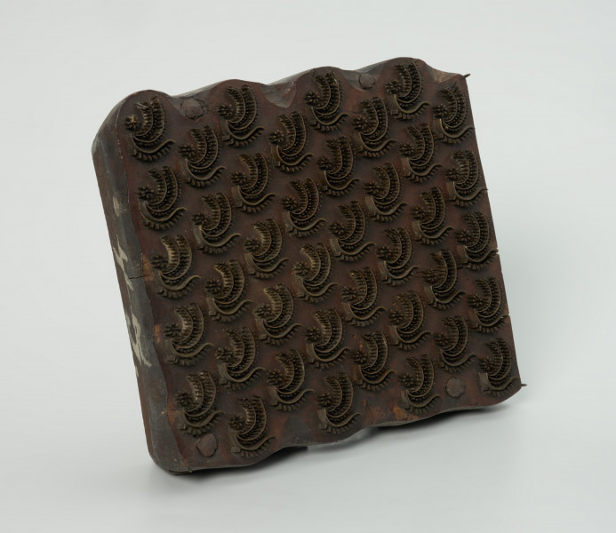 sprzęt do drukowania i grafiki, matryca drukująca - Ujęcie przodu skosem w lewą stronę. Matryca do drukowania tkanin z wykonanym z nabitych w drewno mosiężnych sztyfcików i blaszek ornamentem o motywie roślinnym.