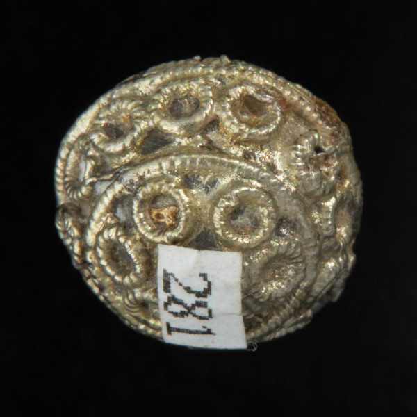 Pozłacany guz kulisty - Ujęcie spodu guzka. Pozłacana ozdoba kolista; na blaszanej kuli pasma kółeczek, rozdzielonych pierścieniami z perełkowanego drutu. Na górze, na środku okrągła granulka.