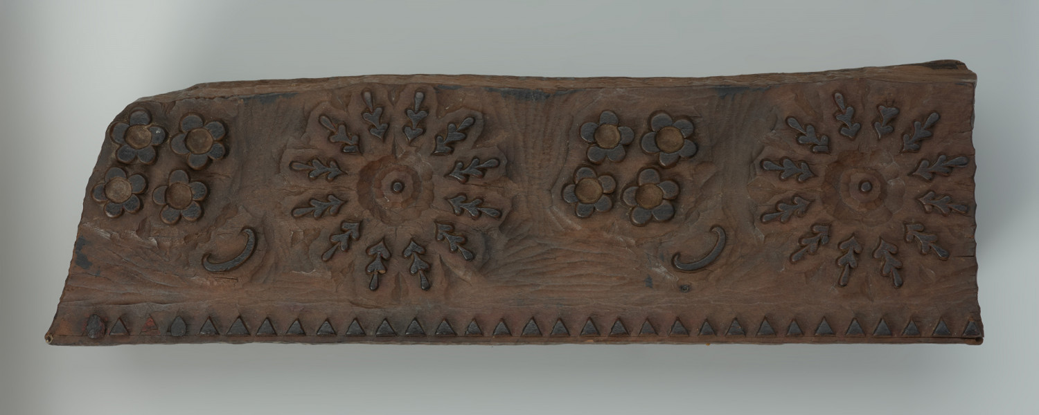 sprzęt do drukowania i grafiki, matryca drukująca - Ujęcie z przodu w pionie na dłuższym boku. Matryca do drukowania tkanin z wykonanym w drewnie ornamentem o motywie geometryczno - roślinnym.