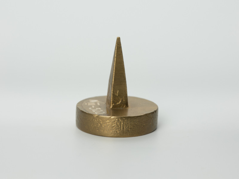 tłok pieczętny - Ujęcie w pionie trzpieniem do góry lekko w prawą stronę. Okrągły tłok pieczętny z brązu z trzpieniem montarzowym w formie ostrosłupa oraz rysunkiem gryfa na iglicy wieży w polu pieczęci.