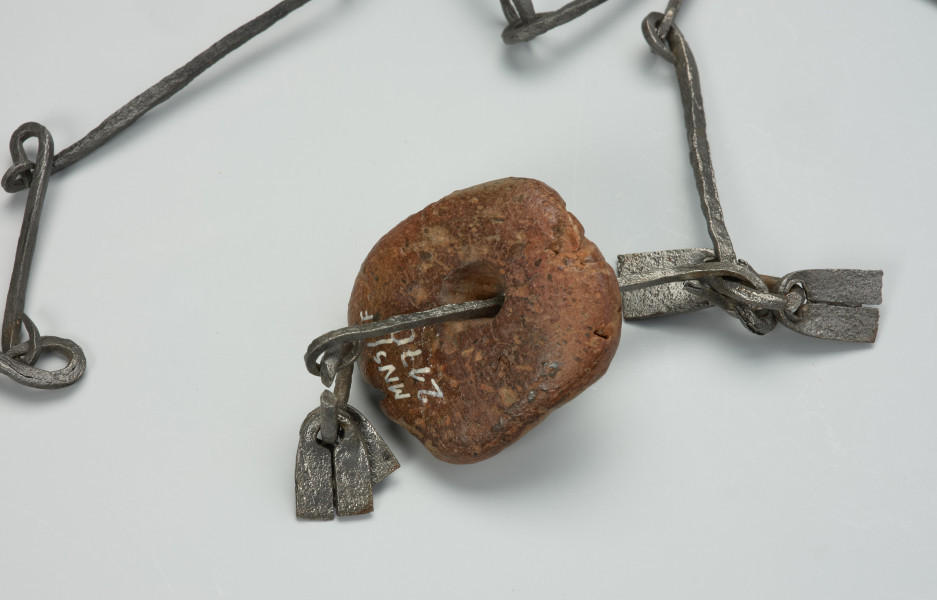 przedmiot ceremonialny, przedmiot religijny i obrzędowy, fetysz - Ujęcie detalu. Łańcuch składający się z licznych, połączonych ze sobą żelaznych ogniw. Rozdwaja się na końcu tworząc literę Y. Ozdobiony pierścieniami z podwójnym wisiorkiem o trapezowatym kształcie, kamiennym i żelaznym paciorkiem oraz otwartym, żelaznym walcem.