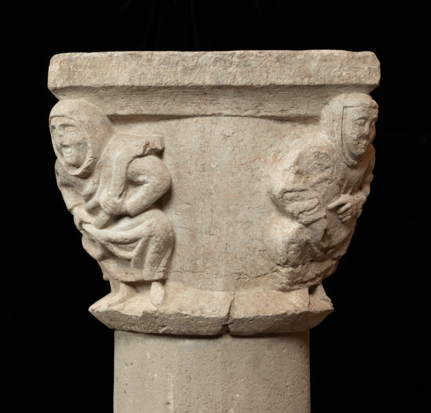 Kapitel z przedstawieniem czterech mnichów - atlantów - Ujęcie czwartejgo boku. Kapitel blokowo-kielichowy, rozszerzający się ku górze, wykuty z jednego kawałka kamienia. Okrągłą podstawę otacza wałek o trójkątnym profilu. Zwieńczenie w formie szerokiej czworobocznej płyty abakusa. W narożnikach kapitela płaskorzeźbione wizerunki czterech mnichów. Postaci o krępej budowie ukazane frontalnie, w pozycji przykucniętej. Stopami opierają się o dolny wałek, głowami podpierają abakus. Relief głęboki, półplastyczny, światłocieniowy. Gładko opracowane tło. Niewielkie uszczerbienia zwłaszcza w partii abakusa i dolnego wałka. Pod spodem centralne wgłębienie do umocowania trzpienia łączącego kapitel z trzonem.