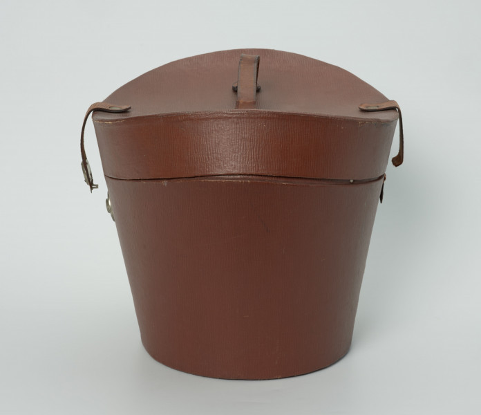 owalny futerał do kapelusza - Ujęcie z boku; Owalny futerał do kapelusza. Owalne, rozszerzające się ku górze pudło z pokrywą o zagłębionej formie z uchwytem w centrum. Pokrywa zamykana na zamek kluczykowy.