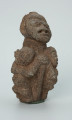 rzeźba; przedmiot obrzędowy; figura kultu zmarłych - Ujęcie z przodu z prawej strony. Rzeźbiona w ziemistym steatycie siedząca postać ludzka o cechach kobiecych, otoczona przez trójkę mniejszych, dzieciecych postaci, skierowanych ku niej z uniesionymi rękoma.