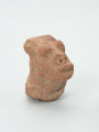 głowa - Ujęcie ze skosu z prawej; Gliniana głowa postaci ludzkiej o ceglastym kolorze i prostokątnej twarzy, która opiera się na masywnej szyi. Zachowało się lewe ramię, na którym wymodelowano charakterystyczną ozdobę w kształcie koła, od którego odchodzą promienie. Figurce zaznaczono rysy twarzy: wydatne, rozchylone usta, szeroki nos o okrągłych nozdrzach oraz wypukłe, okrągłe oczy, które przypominają dwie kulki gliny. Na głowie postaci zaznaczono dwa okrągłe zgrubienia (guzki), które prawdopodobnie przedstawiają fryzurę lub nakrycie głowy. Na powierzchni widoczne są rysy, mikropęknięcia oraz przetarcia.