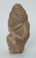 rzeźba; przedmiot obrzędowy; Figura kultu zmarłych - Ujęcie lewy bok. Rzeźbiona w szarobeżowym steatycie postać ludzka ze spiralną linią na czubku dużej głowy, siedząca z przykurczonymi nogami i trzymająca w dłoniach bliżej nieokreślone przedmioty, kształtem przypominające motyki.