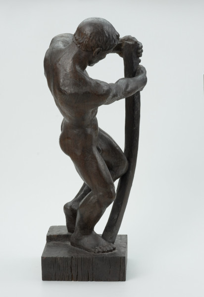 akt męski - Ujęcie z boku z lewej strony; Akt męski ujęty w kontrapoście. Tors odchylony w lewo, wyciągnięte w prawo ręce obejmują wygiętą w łuk belkę, wspartą drugim końcem na postumencie. Stopy złączone, kolana przygięte, rozchylone, jedno z kolan napiera na belkę. Krągła głowa pochylona w dół, włosy krótkie, przylegające do czaszki.