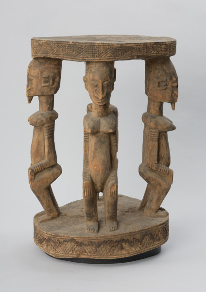 rzeźba - Ujęcie z przodu z lewej strony. Drewniany stół. Okrągły blat połączony z podstawą o tym samym kształcie za pomocą czterech rzeźbionych postaci.