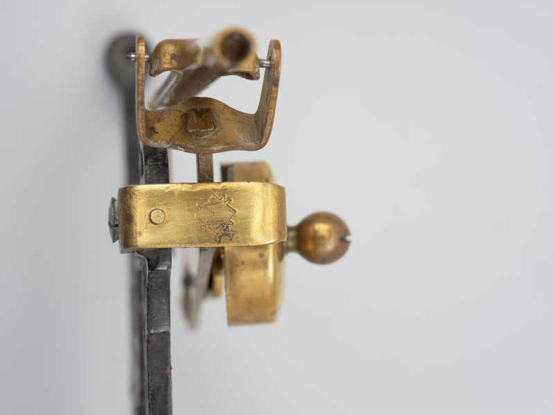 jednowahadłowa uchylna waga pocztowa - detal;  Jednowahadłowa uchylna waga pocztowa. Na głównej dźwigni wagi w kształcie rombu, w środku znajduje się znak litera 