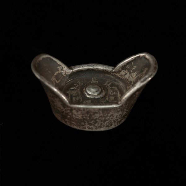 liang , tael - Ujęcie skosem z góry. Sztabka w kształcie łódki z chińskimi napisami na dolnej i górnej stronie.