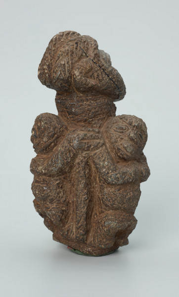 rzeźba; przedmiot obrzędowy; figura kultu zmarłych - Ujęcie z tyłu z prawej strony. Rzeźbiona w ziemistym steatycie siedząca postać ludzka o cechach kobiecych, otoczona przez trójkę mniejszych, dzieciecych postaci, skierowanych ku niej z uniesionymi rękoma.