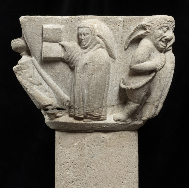 czarci kapitel - Ujęcie zakonnicy czytającej książkę i po prawej czarta. Kapitel blokowo-kielichowy, rozszerzający się ku górze, wykuty z jednego kawałka kamienia. Okrągłą podstawę otacza wałek o trójkątnym profilu. Czworoboczne zwieńczenie. Powierzchnia dekorowana płaskorzeźbionymi przedstawieniami pięciu mnichów, stołu eucharystycznego z kielichem i hostią oraz czarta. Postaci o krępej sylwetce i dużych głowach. Brzegi szat dekorowane charakterystycznym podwójnym wałkiem. Czart nagi, o muskularnej budowie, z dużą głową i długimi uszami. Okrągła twarz o migdałowatych oczach, wyszczerzona w szerokim uśmiechu. Relief głęboki, półplastyczny, światłocieniowy. Gładko opracowane tło. Niewielkie obtłuczenia przy podstawie i zwieńczeniu. Brak abakusa. Pęknięcie dookoła kapitela na wysokości powyżej wałka. Pod spodem centralne wgłębienie do umocowania trzpienia łączącego kapitel z trzonem.