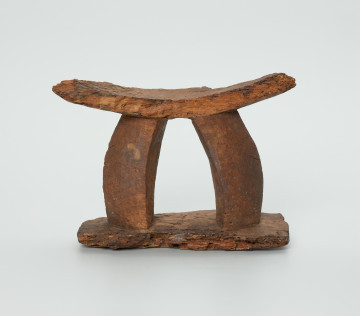 obrządek grzebalny , pochówek , podgłówek - Ujęcie z przodu. Rzeźbiony, drewniany podgłówek pokryty warstwą brunatnej ziemi. Część górna oparta na dwóch łukowatych dźwigarach. Liczne spękania oraz dziurki.